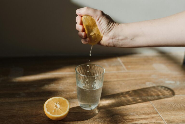 A hand squeezing a lemon into a glass, capturing the fresh juice in natural light.